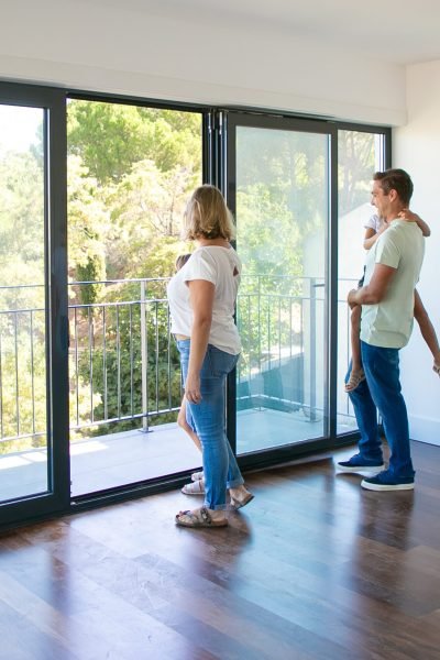 Happy family with kids looking at balcony and smiling. Back view of blonde mother. Daughter sitting on father hands. People watching new house or flat. Mortgage, relocation and moving day concept